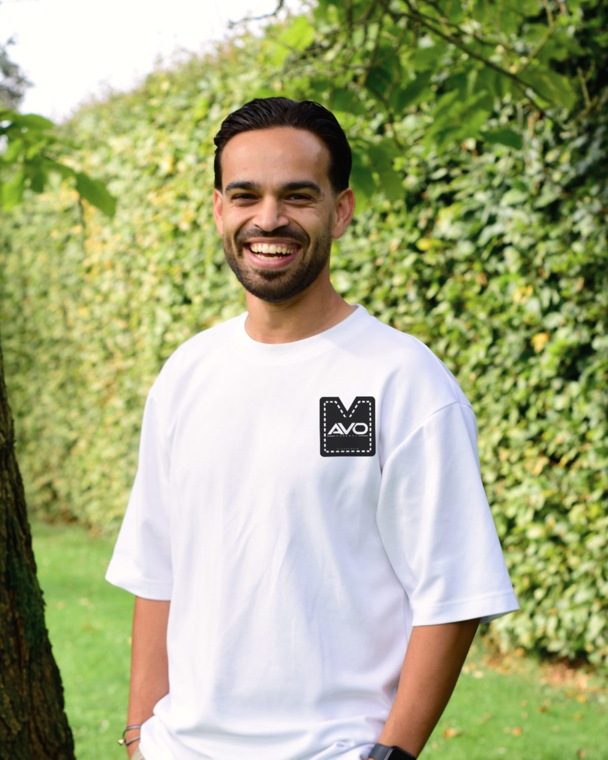Alex van Overdijk lacht in een wit T-shirt met het AVO Workwear-logo op de borst